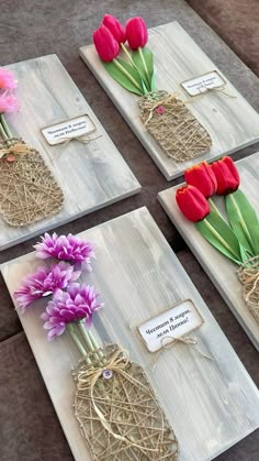 four pieces of wood with flowers in vases and tags attached to them on the table