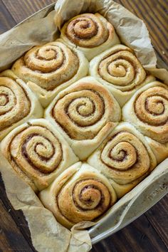 cinnamon rolls in a baking pan on a wooden table with paper wrapping around them and the top one rolled up