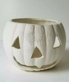 a white ceramic pumpkin bowl with holes in the front and two faces carved into it