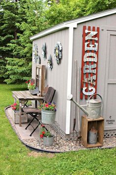 a garden shed with an old sign on the side and flowers in buckets next to it