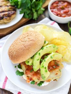 a sandwich with meat, cheese and avocado is on a plate next to potato wedges