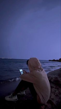 a person sitting on the beach looking at their cell phone in front of the ocean