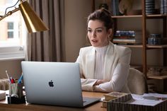 a woman sitting at a desk in front of a laptop computer with an apple logo on the screen