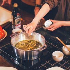 two people preparing food in a pot on top of a stove with wooden spoons