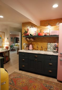 a kitchen with pink refrigerator, black cabinets and yellow brick wall in the back ground