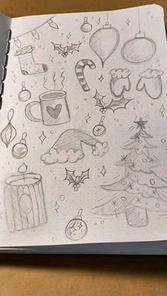 an open notebook with drawings on it and christmas decorations around the page, along with a pen