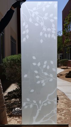 a person is holding up a frosted glass window with white leaves on it in front of a building