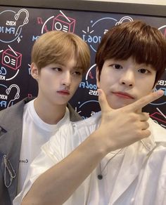 two young men standing next to each other in front of a wall with writing on it