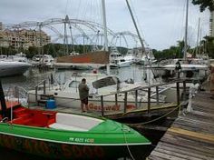 a man standing next to a green and white boat at a dock with other boats in the water