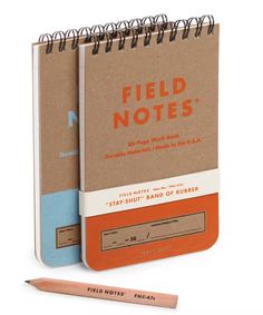 two notebooks with the words field notes written in orange and blue on them next to a pencil