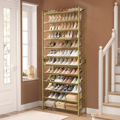 a gold shoe rack with many pairs of shoes on it in front of a staircase