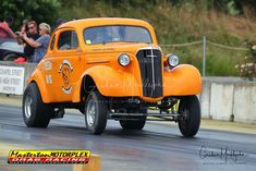 an orange truck driving down a street next to other cars and people watching from the sidelines