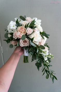 a person holding a bouquet of white and pink flowers in front of a gray wall