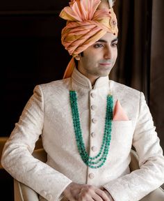 a man wearing a turban and beaded necklaces sits in a chair