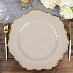 a white plate with gold trim sits on a wooden table next to silverware and flowers