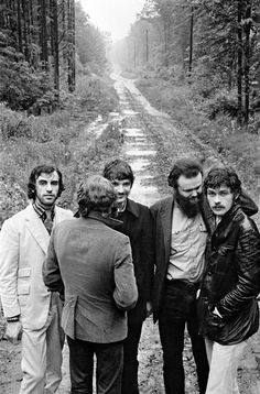 black and white photograph of four men standing in front of a dirt road surrounded by trees