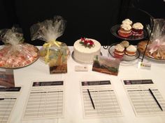 a table topped with cakes and cupcakes covered in frosting next to price tags