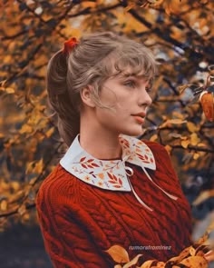 a woman in a red sweater and white collared shirt standing next to a tree with yellow leaves