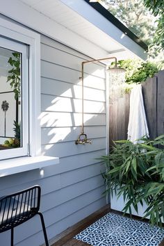 an outdoor shower with plants in the corner and a blue rug on the floor next to it