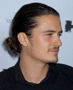 a close up of a person wearing a black shirt with a ponytail in his hair