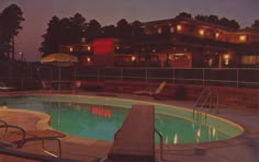 an empty swimming pool at night with chairs and umbrellas