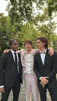 three young men in suits posing for the camera with their arms around each other and trees behind them