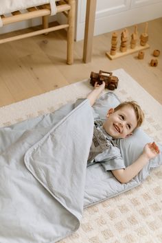 a little boy laying on top of a bed with a blanket over his head and smiling at the camera