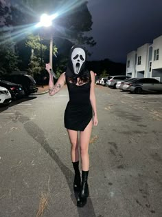 a woman in a black dress and mask walking down the street with a light on her head