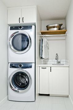 a washer and dryer in a small laundry room with white cabinetry, counter tops, and open shelving