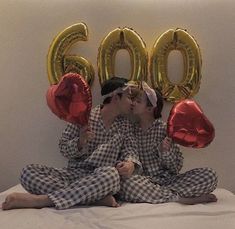 two people sitting on a bed with balloons in front of them and the number 600