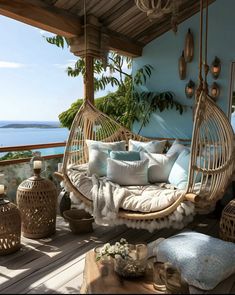 a porch with a swing chair and pillows on the floor next to it, overlooking the ocean