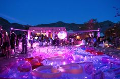 an outdoor party with purple lights and plates on the ground, surrounded by other people