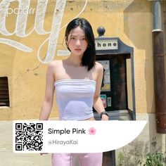 a woman in white top and pink pants standing next to a phone booth with qr code on it