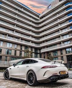 a white sports car parked in front of a large building with balconies on it