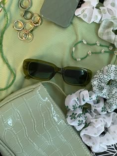 a green purse, sunglasses and other accessories are laying on the ground next to each other