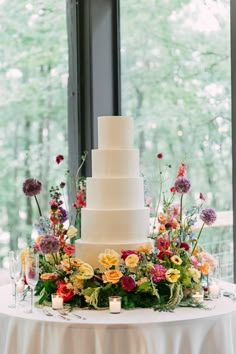 a white wedding cake sitting on top of a table next to a tall glass window