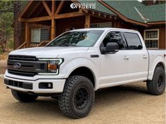 a white truck is parked in front of a log cabin with black tires and rims