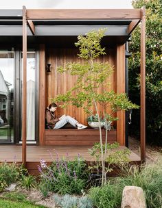 a person sitting on a bench in front of a wooden structure with plants and flowers