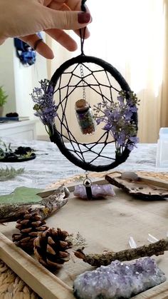 a person holding a piece of wire with pine cones and other things inside it on top of a wooden tray