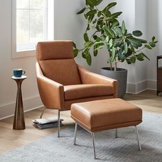 a living room with a chair, ottoman and potted plant