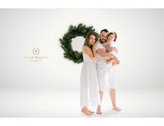 a man and woman holding a baby in front of a christmas wreath