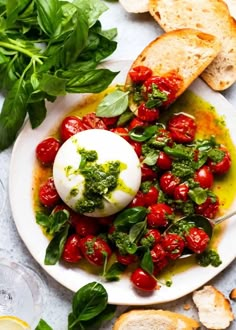 a white plate topped with tomatoes and basil next to slices of bread on top of a table