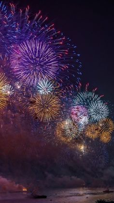 fireworks are lit up in the night sky over water and land with boats on it