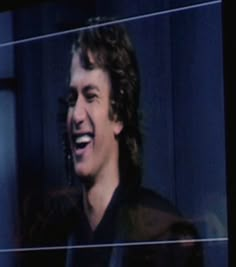 a man with long curly hair laughing in front of a tv screen