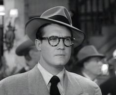 a man wearing glasses and a suit with a hat on his head is looking at the camera