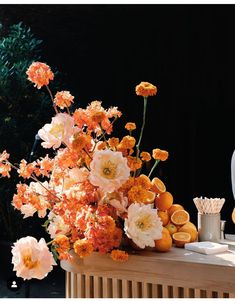 an arrangement of orange and white flowers on top of a wooden table in front of a black background