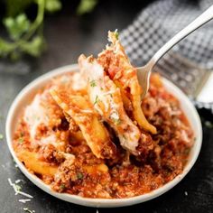 a white bowl filled with pasta and meat covered in sauce on top of a table