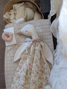 a white stuffed animal sitting on top of a bed next to pillows and blankets in a wicker basket