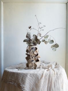 a vase filled with flowers sitting on top of a white table covered in a blanket