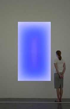 a woman standing in front of a blue square on a wall with another person looking at it